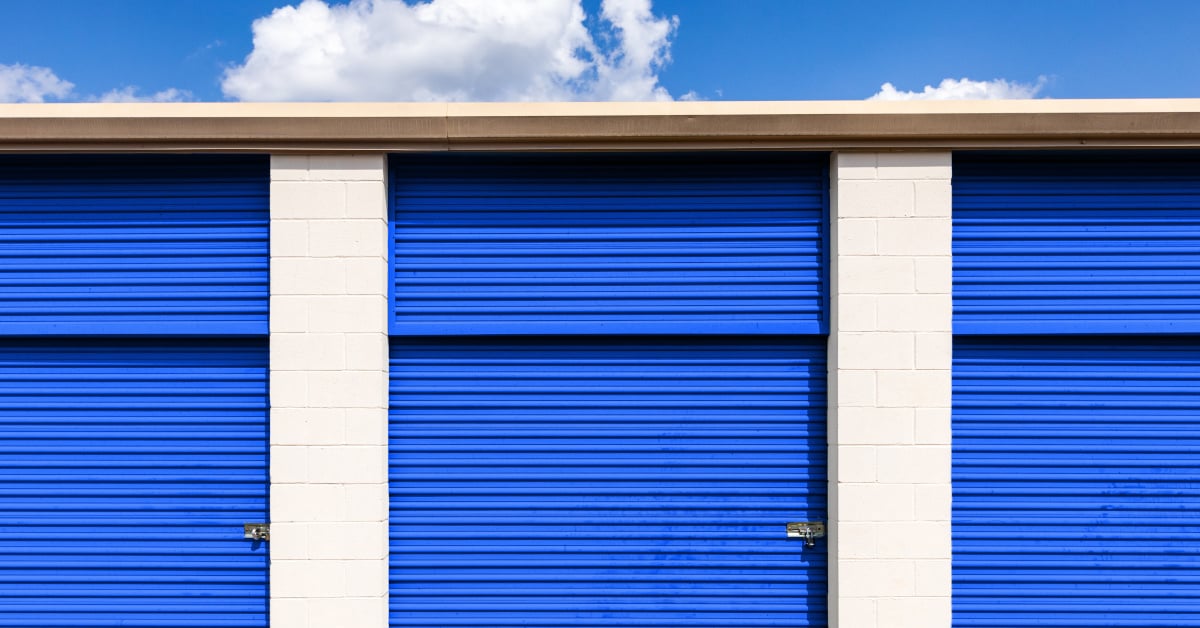 Three self-storage units with blue roll-up doors under a cloudy sky, representing different storage options.