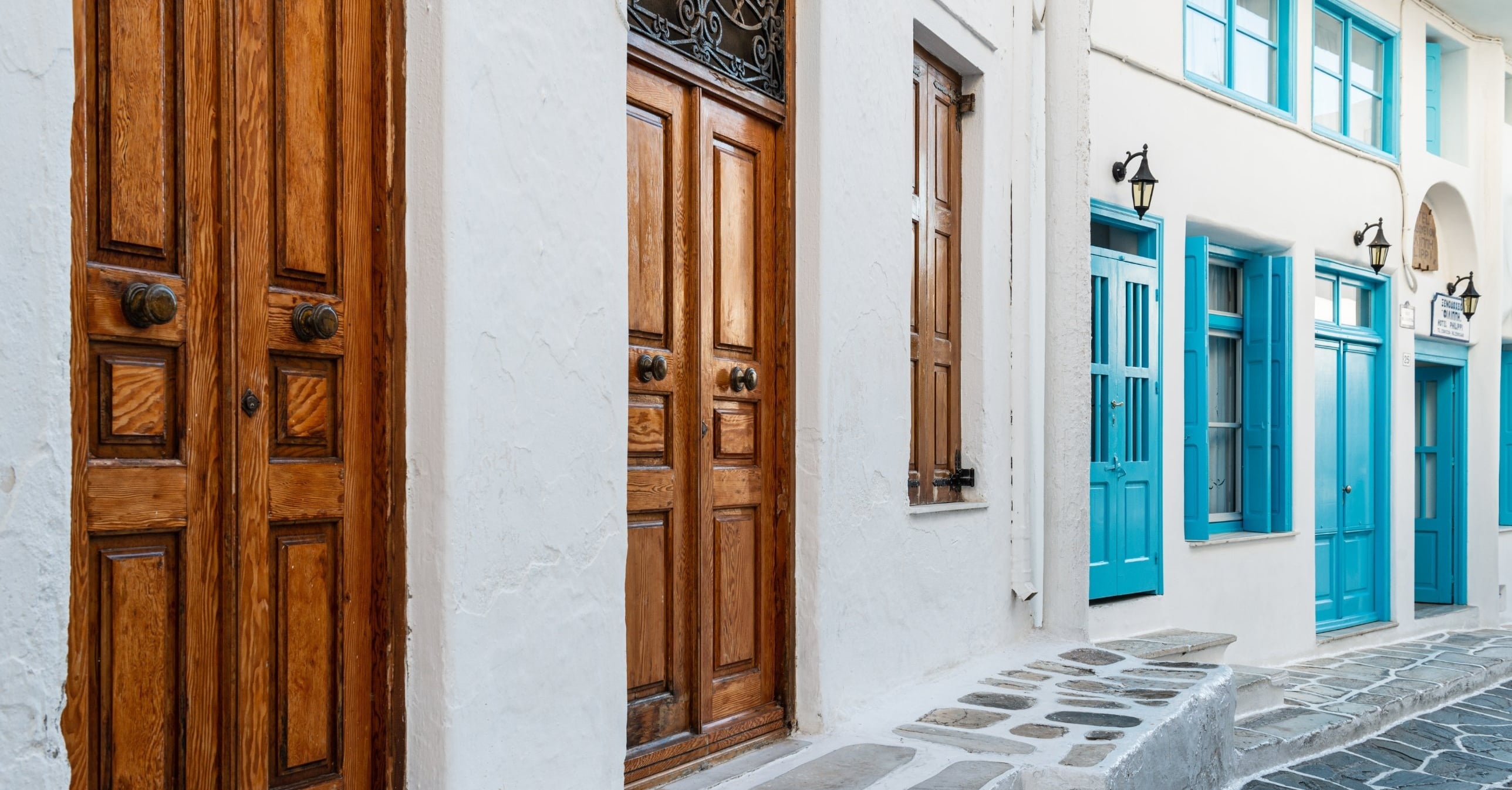 Row of doors along a whitewashed street, with two wooden doors in front and several bright blue doors farther down.